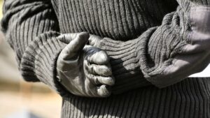 A man wearing a black jumper and gloves, styled on an Irish Republican paramilitary uniform, standing with his hands behind his back in a military pose