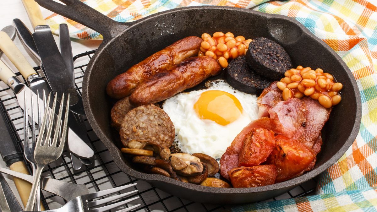 Full Irish breakfast with fried egg, sausages, black pudding, white pudding, baked beans, bacon, tomato and grilled mushrooms in an iron cast skillet